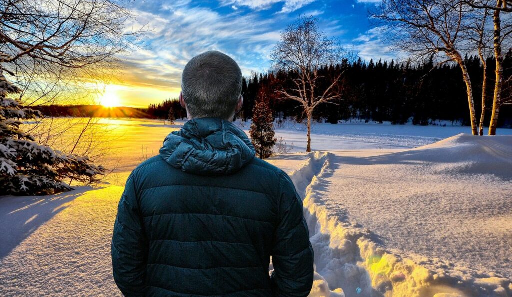 Homme regardant le coucher de soleil hiver